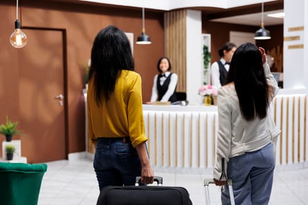 turiste-femminili-che-arrivano-alla-destinazione-portando-bagagli-verso-la-reception-di-un-resort-moderno-turisti-che-iniziano-la-vacanza-nella-lobby-di-un-hotel-stravagante-pronti-fare-la-prenotazione
